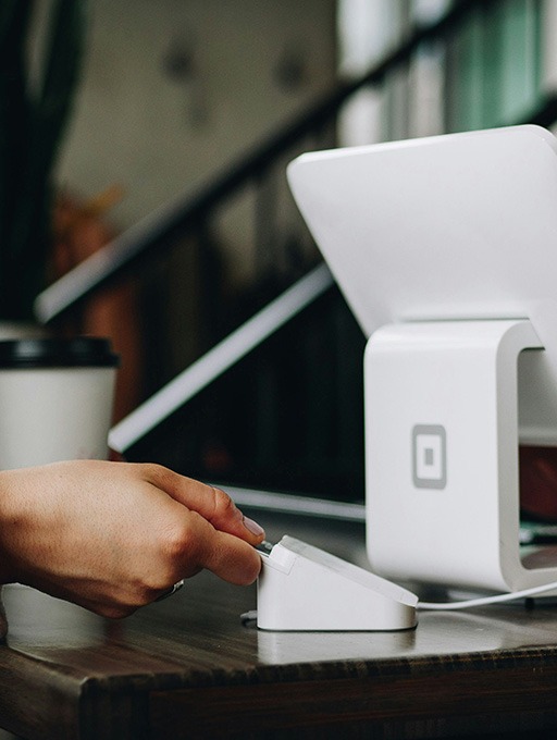 business ready to scale Close-up of a person swiping a credit card at a modern point-of-sale system in a small business setting, with a coffee cup in the background, emphasizing efficient payment solutions for business growth.